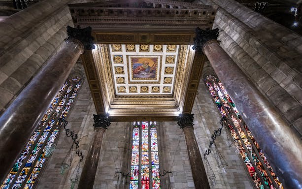 Interior view of Milan Duomo ceiling with stained glass windows and ornate columns.