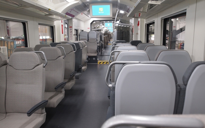 Interior of KLIA Ekspres train with empty seats and digital screens.