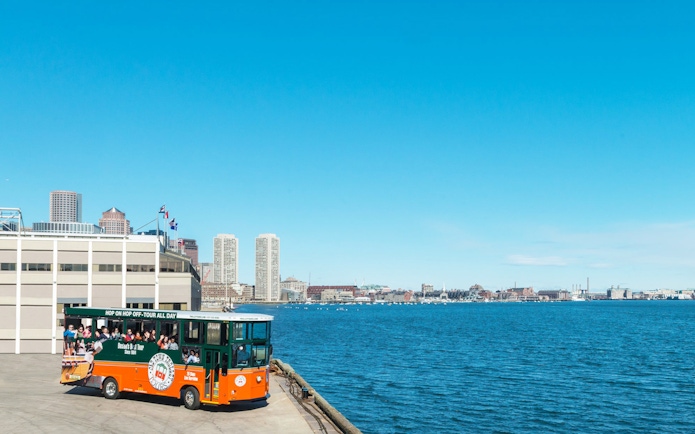 Boston Old Town Trolley by the waterfront with city skyline in the background.