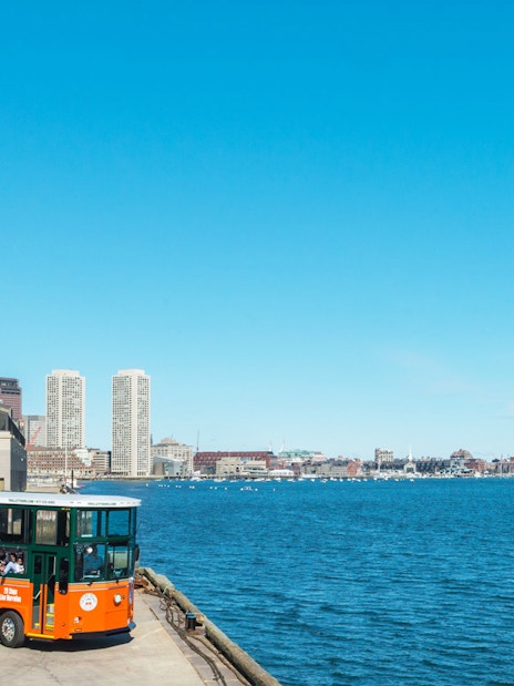 Boston Old Town Trolley by the waterfront with city skyline in the background.