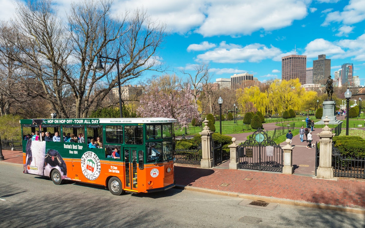 Boston Old Town Trolley passing Boston Public Garden with city skyline in background.