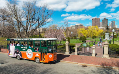 Boston Old Town Trolley passing Boston Public Garden with city skyline in background.