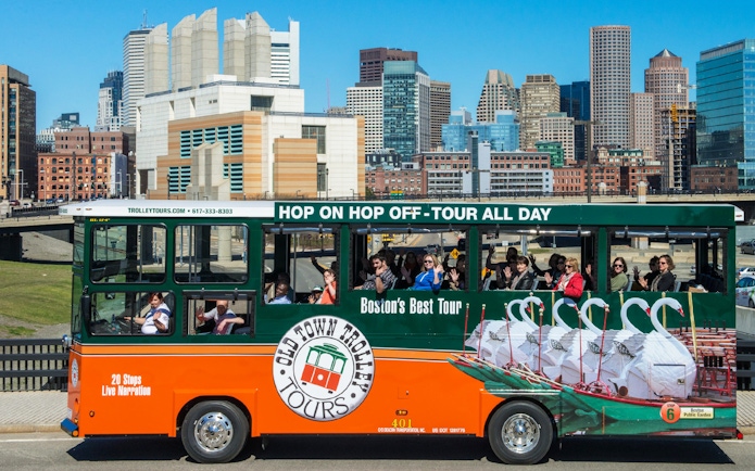 Boston Old Town Trolley with tourists, city skyline in background.