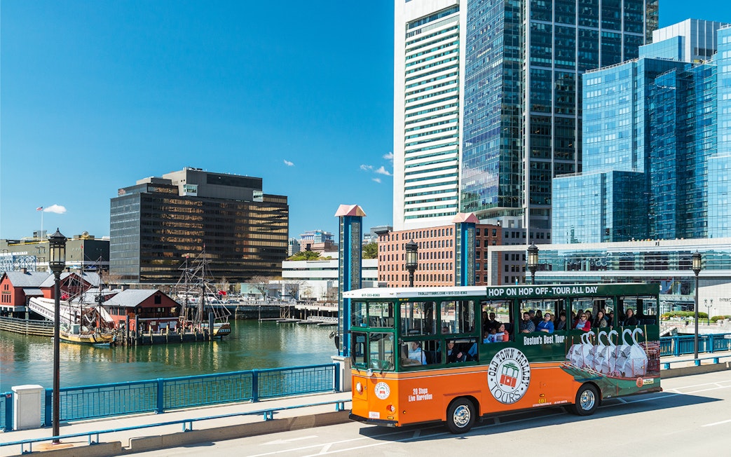 Boston Old Town Trolley passing by the waterfront with city skyline in the background.