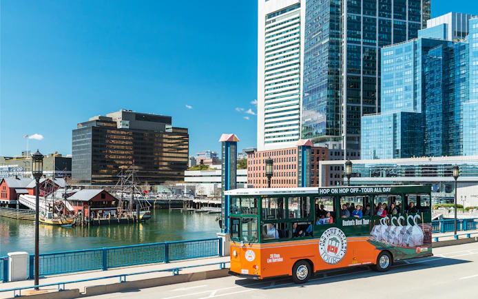 Boston Old Town Trolley passing by the waterfront with city skyline in the background.