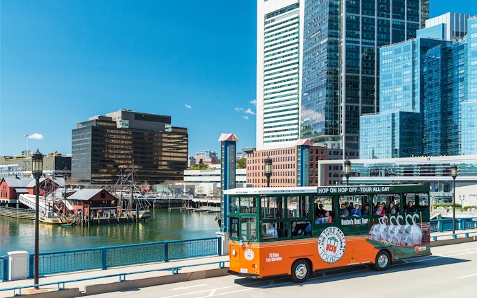Boston Old Town Trolley passing by the waterfront with city skyline in the background.