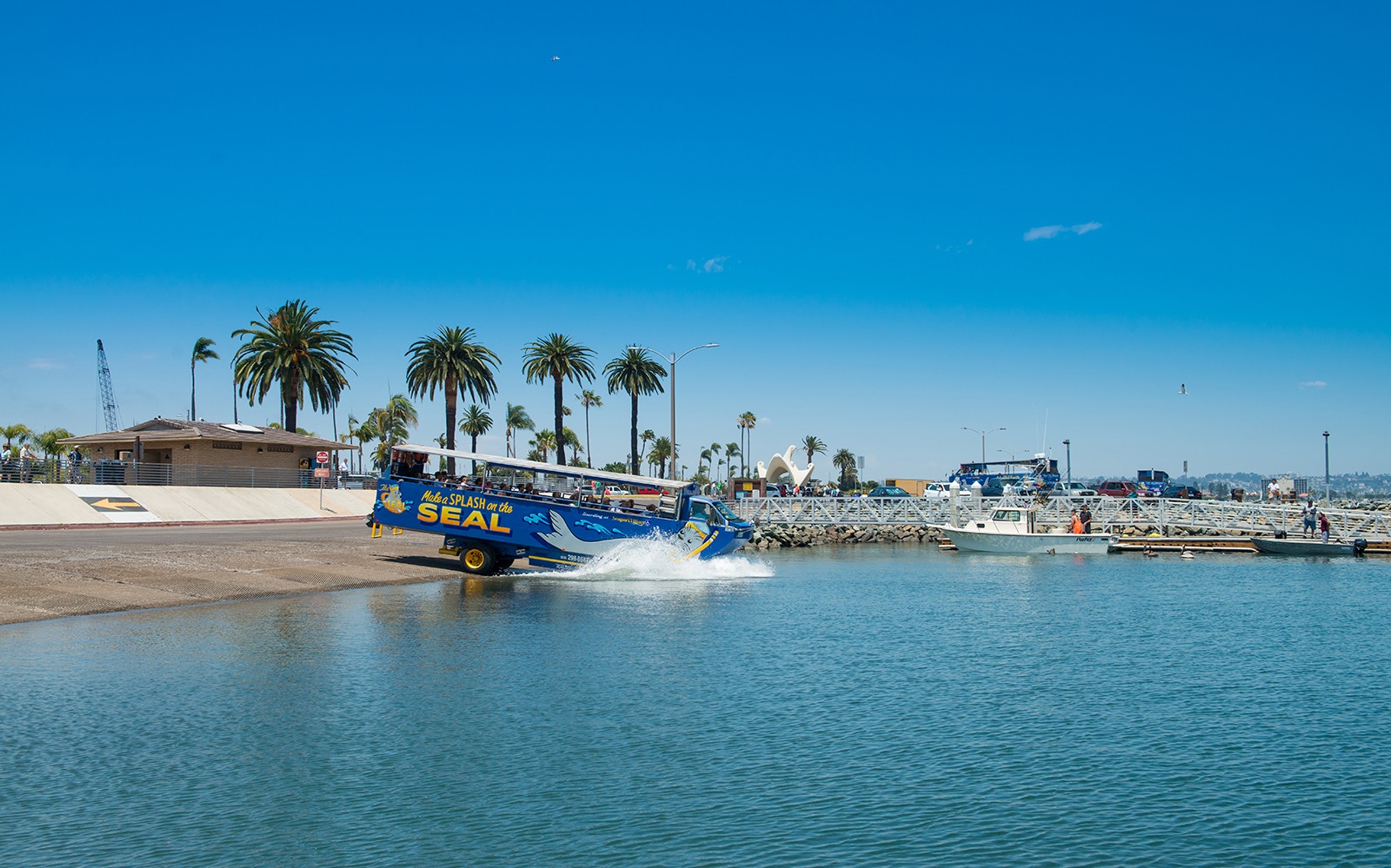 Amphibious vehicle entering water on San Diego SEAL Tour with palm trees in background.