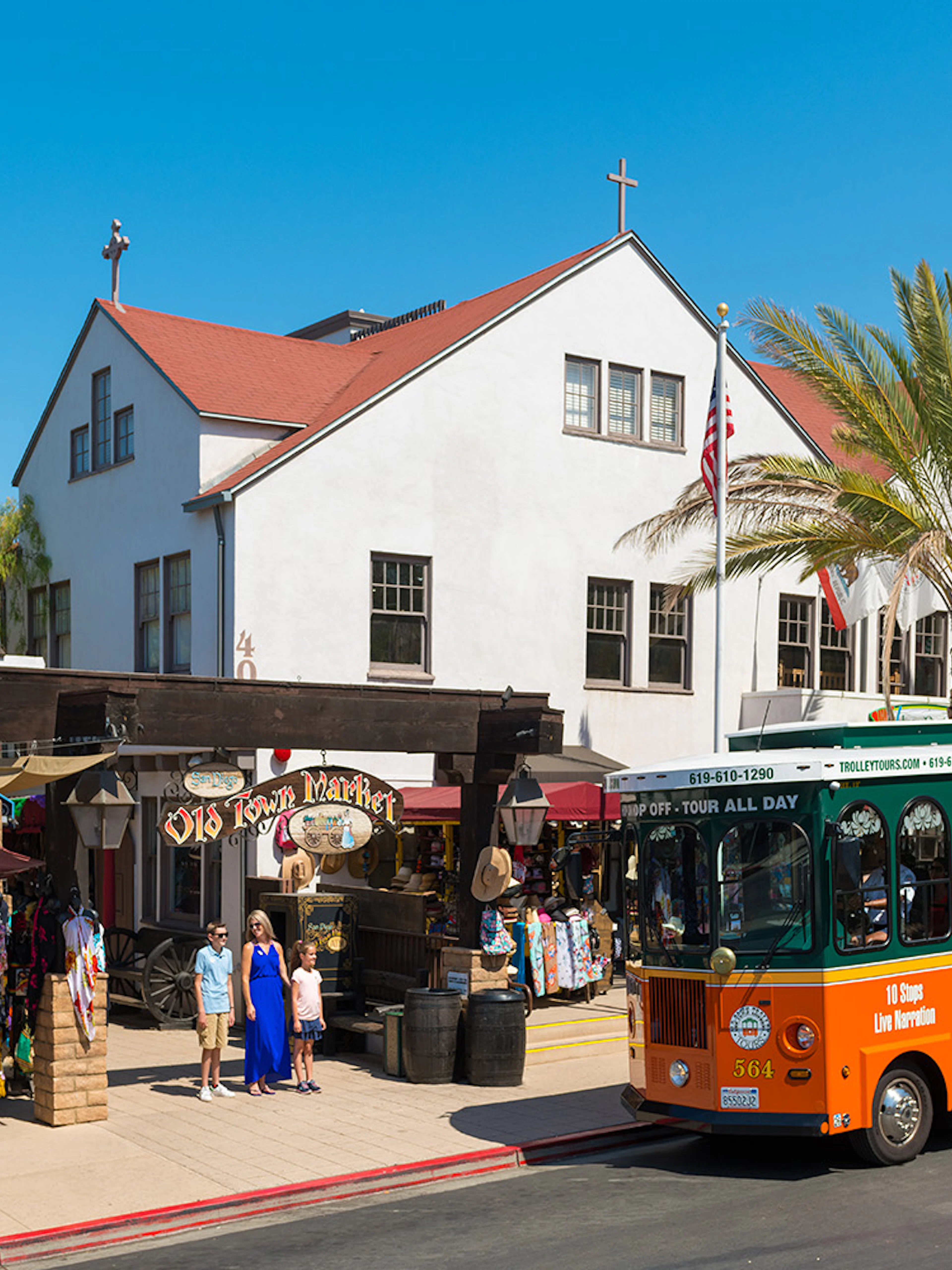 Old Town Trolley in front of Old Town Market, San Diego, with tourists exploring shops.