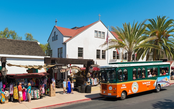 Old Town Trolley in front of Old Town Market, San Diego, with tourists exploring shops.