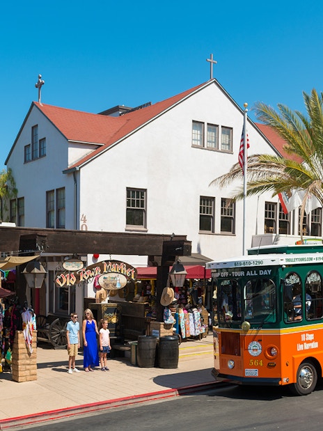 Old Town Trolley in front of Old Town Market, San Diego, with tourists exploring shops.