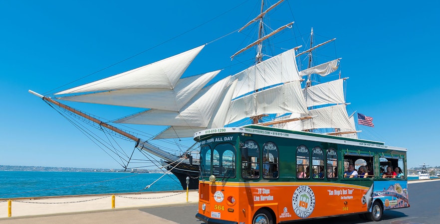 San Diego Old Town Trolley passing a historic sailing ship by the waterfront.