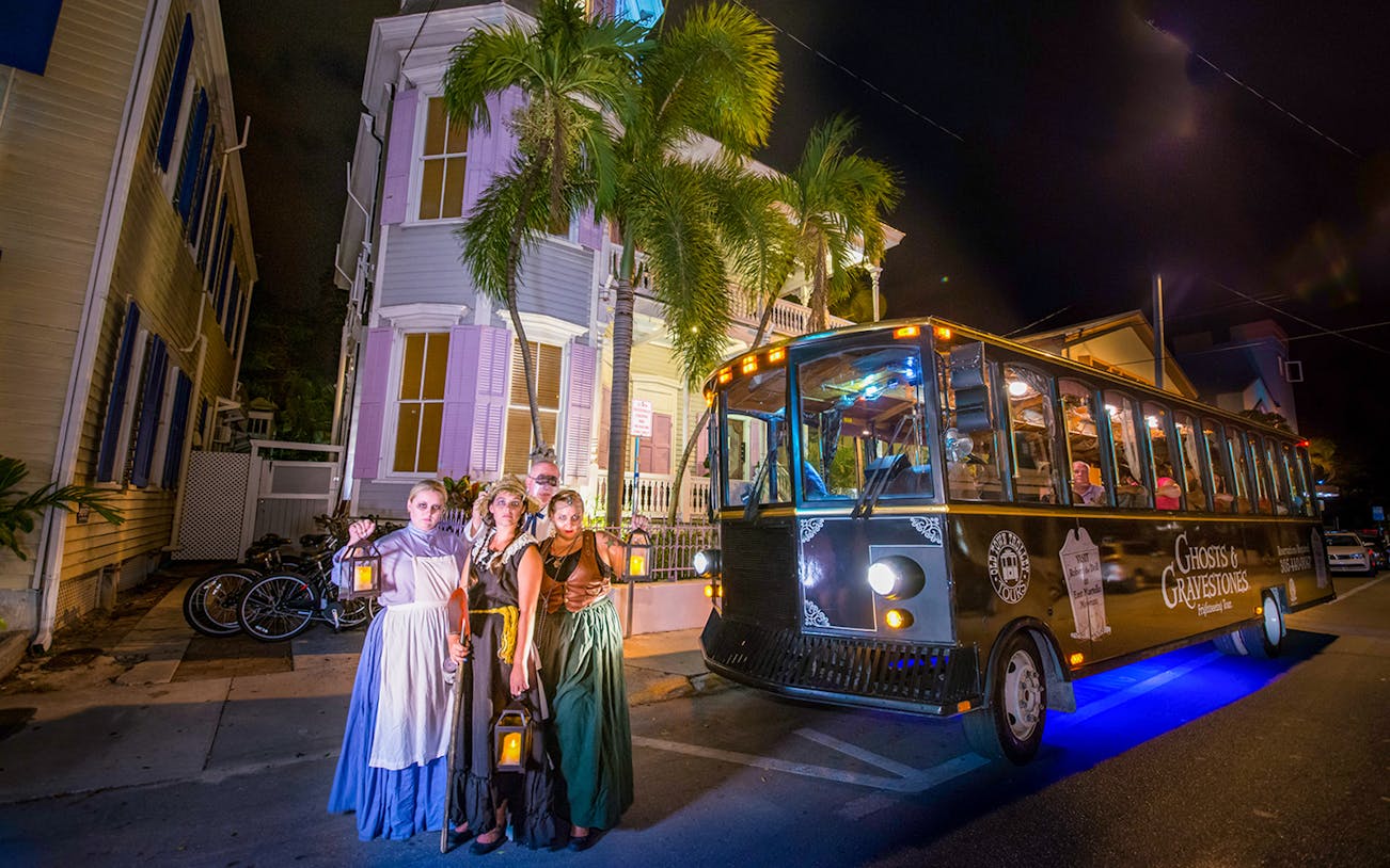 Guided tour group with lanterns beside Ghosts & Gravestones trolley in Savannah at night.