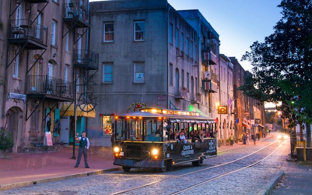 Savannah trolley on cobblestone street during Ghosts & Gravestones tour at dusk.