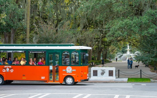 Trolley tour passing through Savannah's historic Forsyth Park with fountain in view.