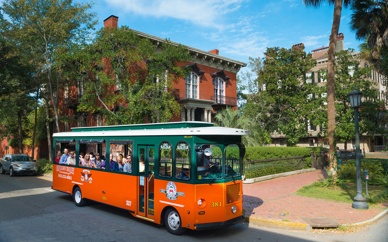 Savannah trolley with tourists passing historic brick buildings in Old Town.