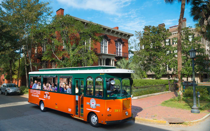 Savannah trolley with tourists passing historic brick buildings in Old Town.