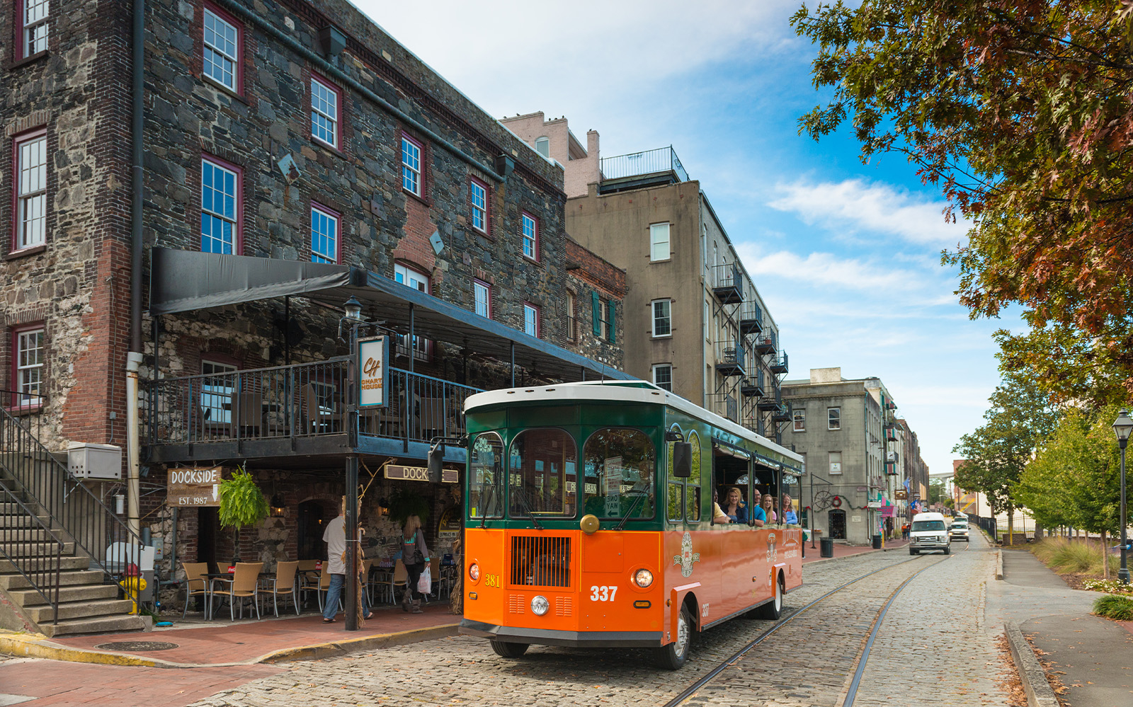 Savannah trolley on cobblestone street near historic buildings.