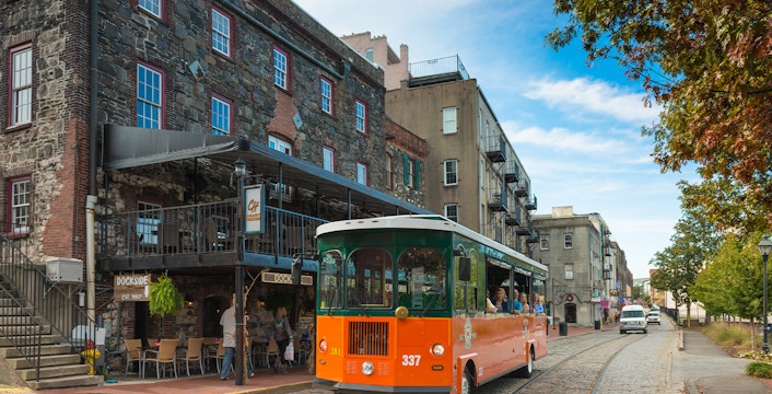 Savannah trolley on cobblestone street near historic buildings.