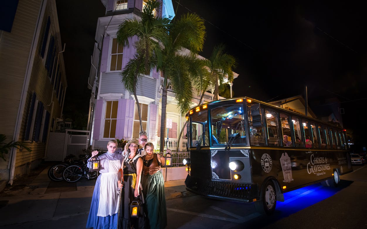 Ghosts & Gravestones tour bus with costumed guides in front of a historic building at night.