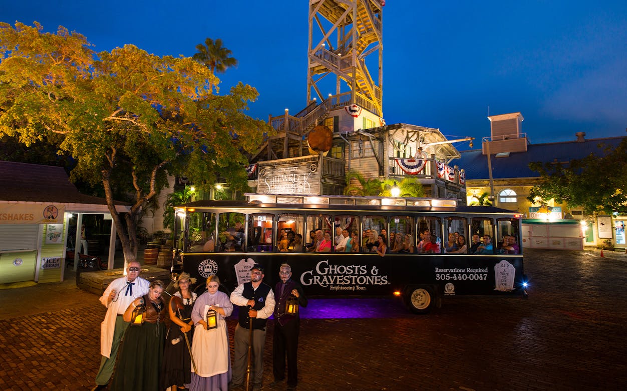 Ghosts & Gravestones tour bus with costumed guides in front of a historic building at night.