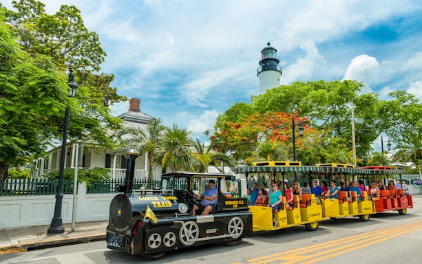 Guided Conch Tour Train passing Key West Lighthouse with tourists onboard.