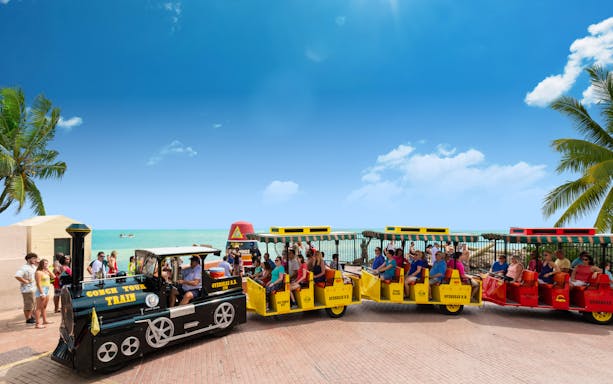 Guided Conch Tour Train with tourists in Key West near the ocean.