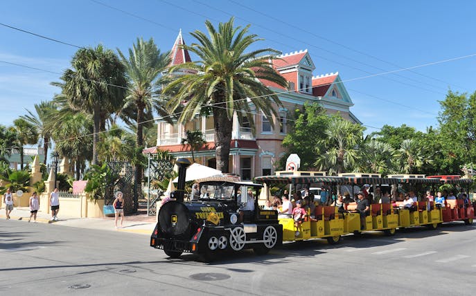 Conch Tour Train passing historic house in Key West.