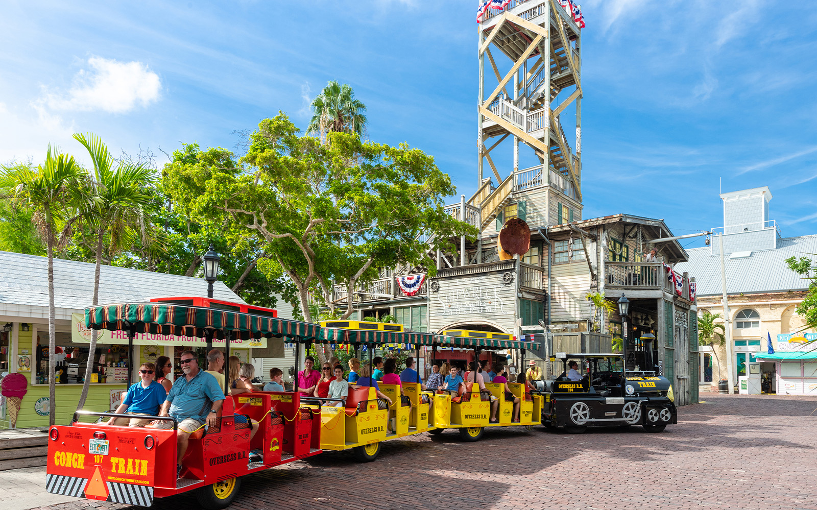 Guided Conch Tour Train with passengers in Key West near historic building.