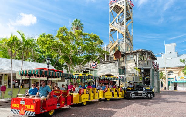 Guided Conch Tour Train with passengers in Key West near historic building.
