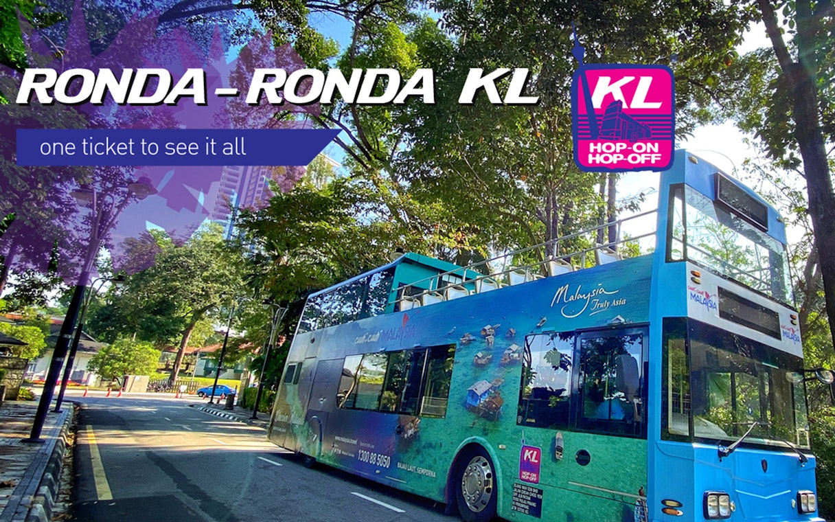 Kuala Lumpur hop-on hop-off bus on a tree-lined street, promoting city sightseeing.