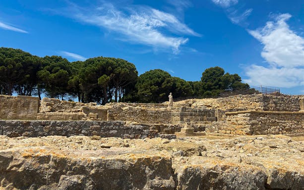 Ancient stone ruins of Empúries with trees in the background under a blue sky.