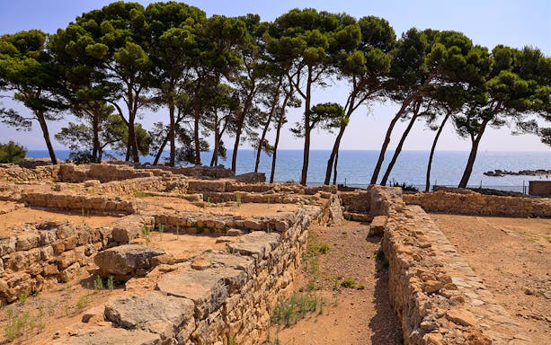 Ancient stone ruins of Empúries with sea and trees in the background, Costa Brava, Spain.