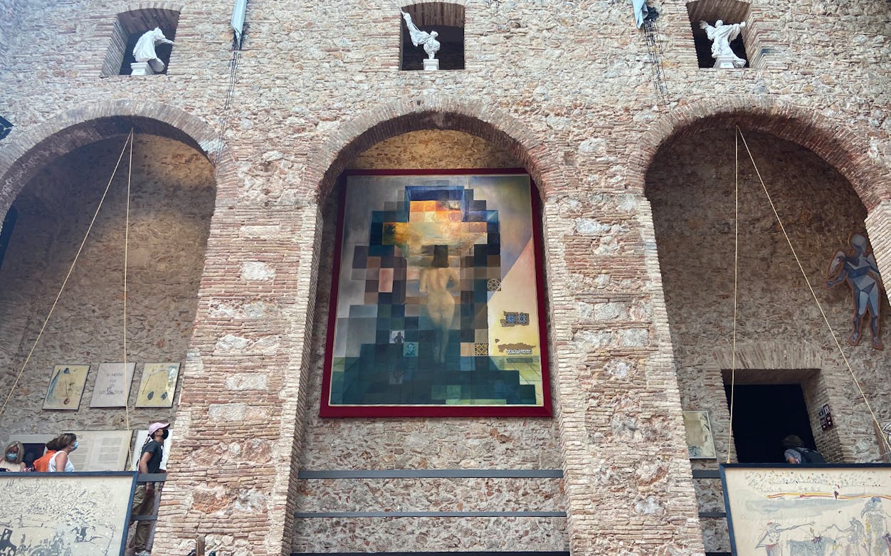 Dalí Museum tour with visitors viewing a large surrealist painting on a brick wall.