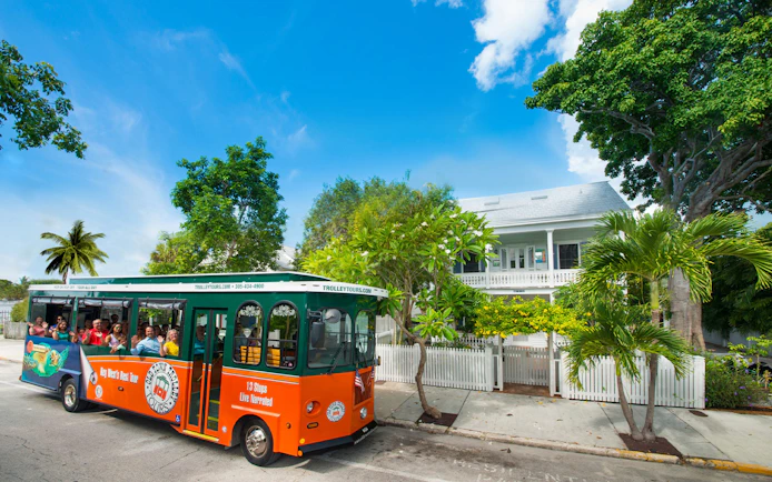 Key West Old Town Trolley passing a historic house with lush greenery.