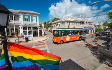 Key West Old Town Trolley passing colorful shops and rainbow flag on a sunny street.