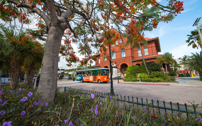 Key West Old Town Trolley passing a historic red brick building with vibrant trees.
