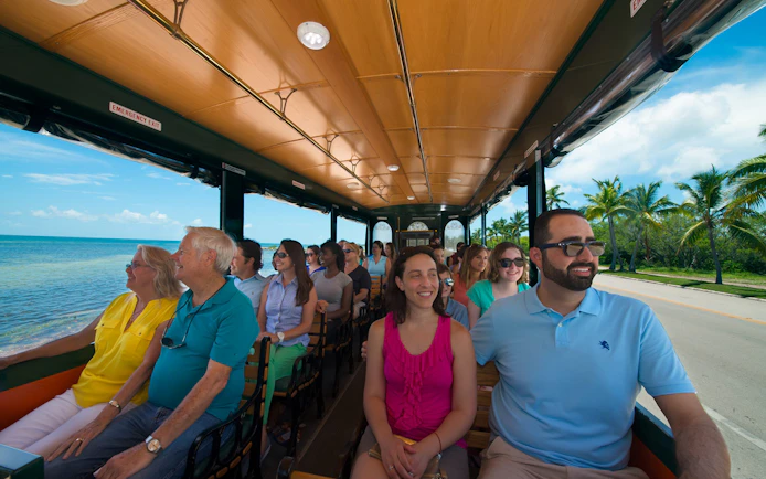 Tourists enjoying a ride on the Key West Old Town Trolley with ocean views.