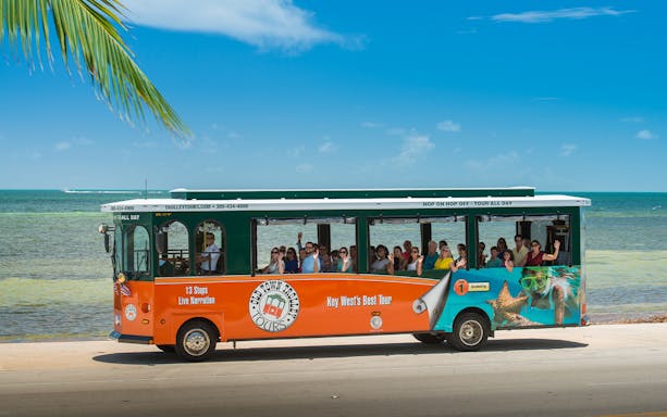 Key West Old Town Trolley with tourists by the ocean.