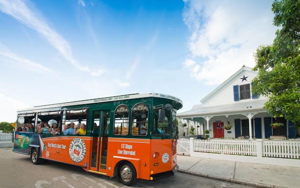 Key West Old Town Trolley passing a historic house with tourists onboard.
