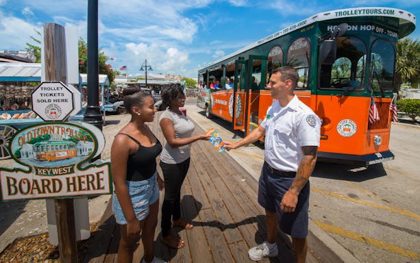 Key West Old Town Trolley guide handing tickets to tourists at boarding area.