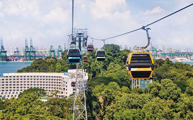 Cable cars over lush greenery with cityscape in the background, Singapore.