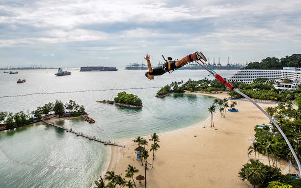 Bungy jumper over Sentosa beach with view of ships and coastline, AJ Hackett Bungy Jump.