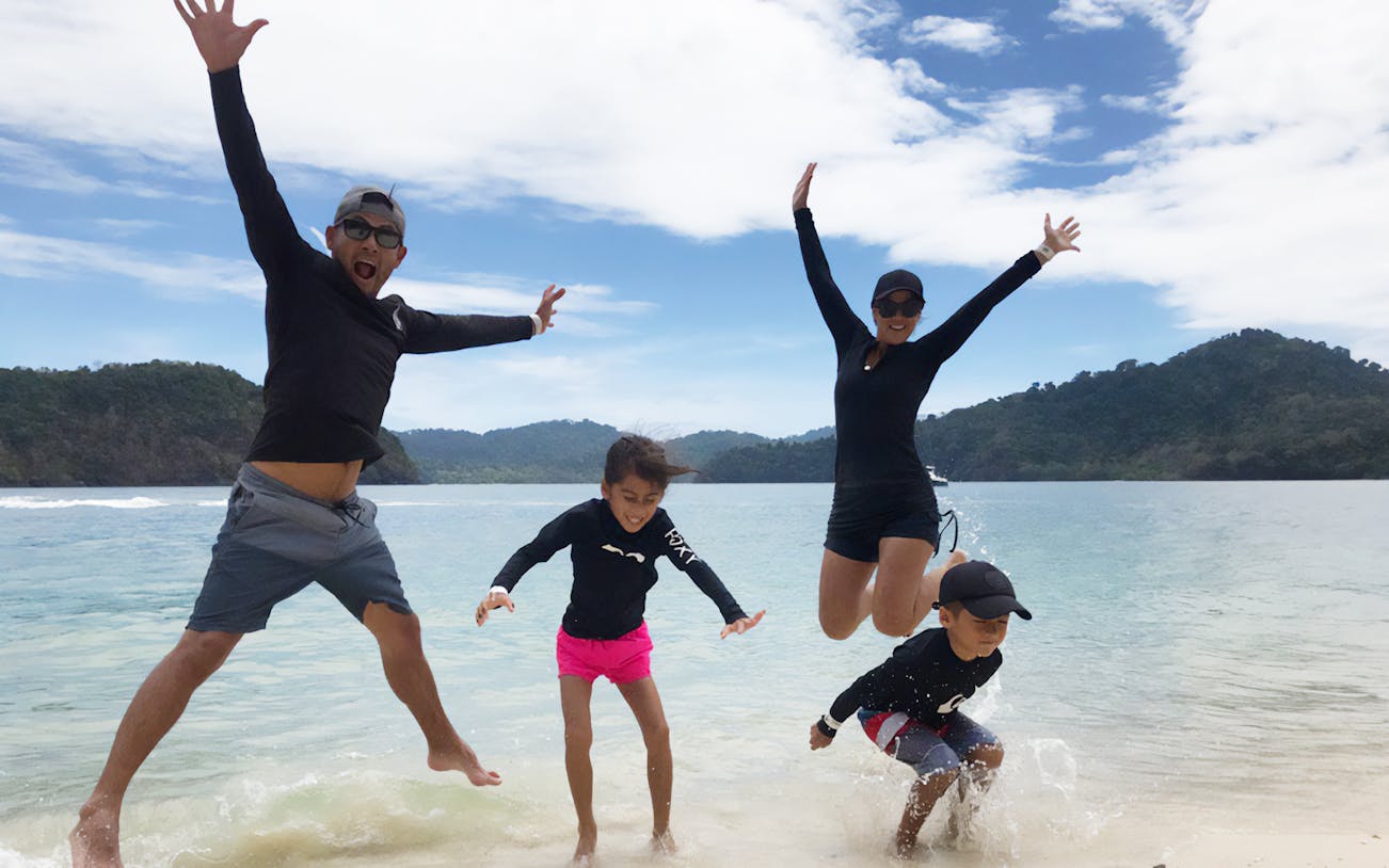Family enjoying the beach on Langkawi Intan Kecil Island with lush hills in the background.
