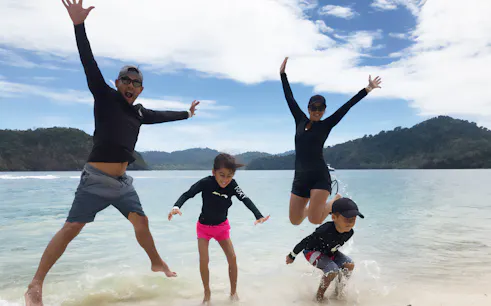 Family enjoying the beach on Langkawi Intan Kecil Island with lush hills in the background.