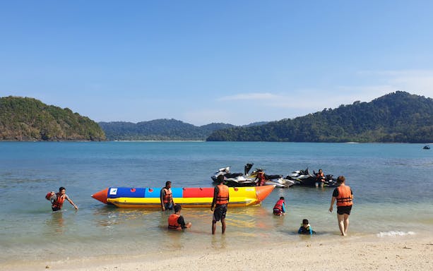 People enjoying a banana boat ride at Intan Kecil Island, Langkawi, with lush hills in the background.