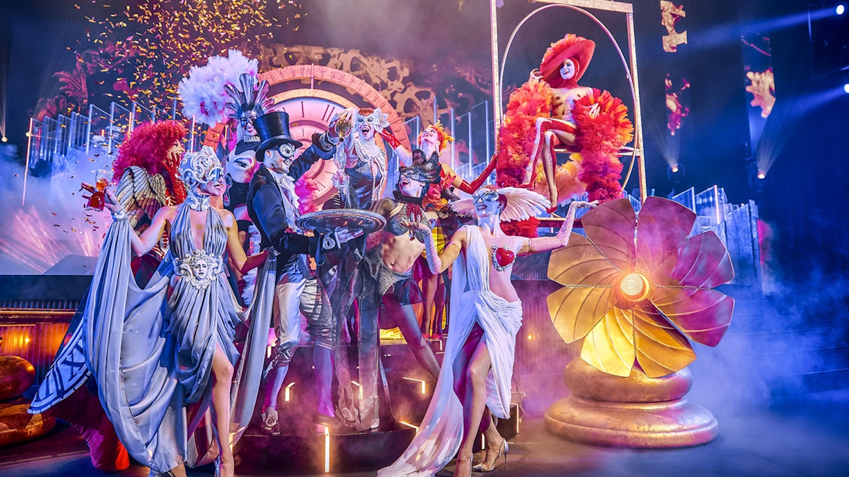 Ensemble aus maskierten Künstlern in extravaganten Kostümen auf einer farbenfrohen Showbühne im Friedrichstadt-Palast