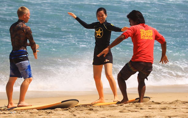 Surf instructor teaching two students on the beach at Odysseys Surf School.