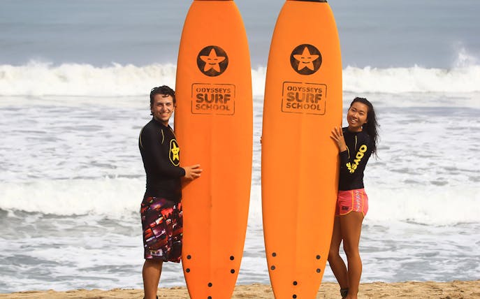 Surfers holding boards at Odysseys Surf School beach lesson.