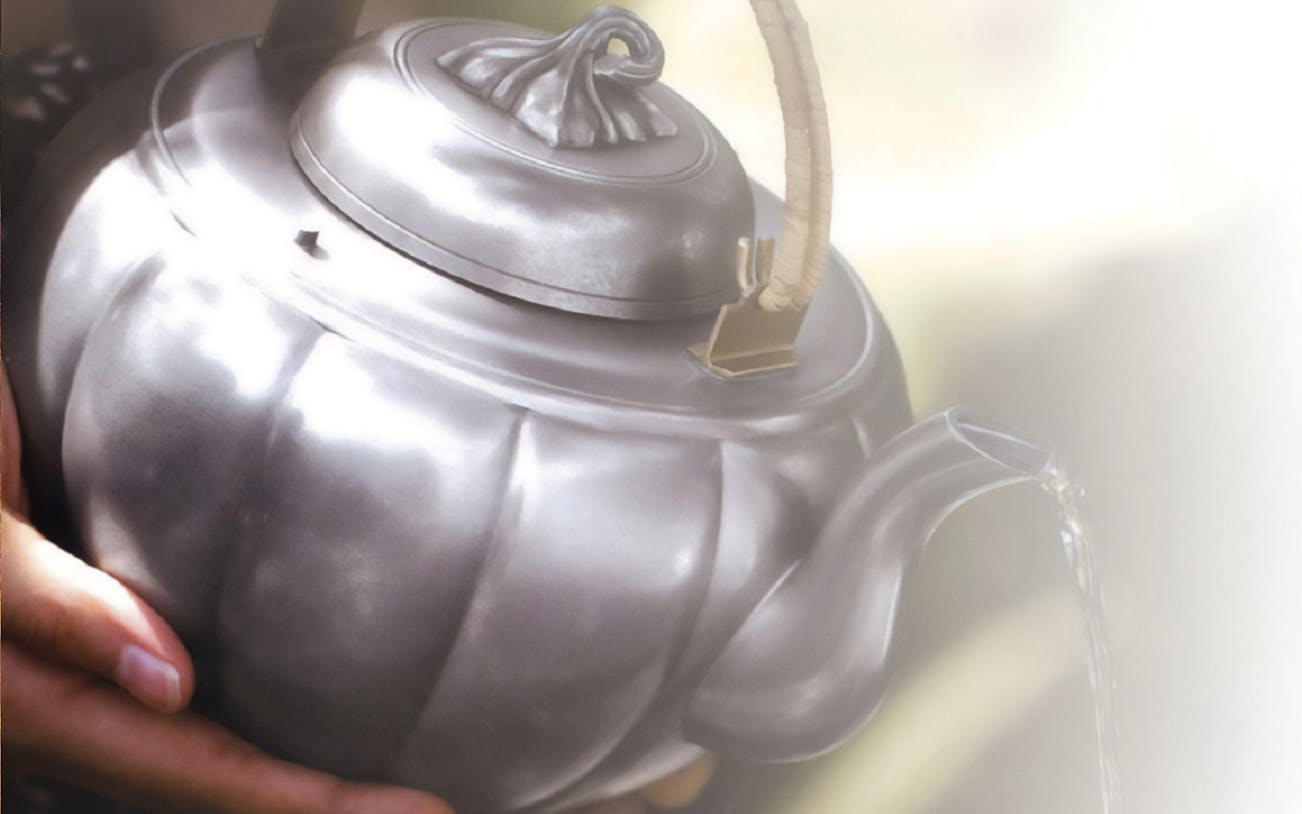 Pouring tea from a metal teapot during Kuala Lumpur countryside tour.
