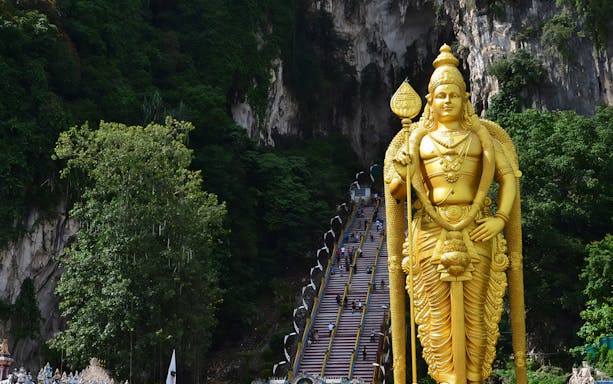 Golden statue of Lord Murugan at Batu Caves entrance, Kuala Lumpur, with steep staircase in background.